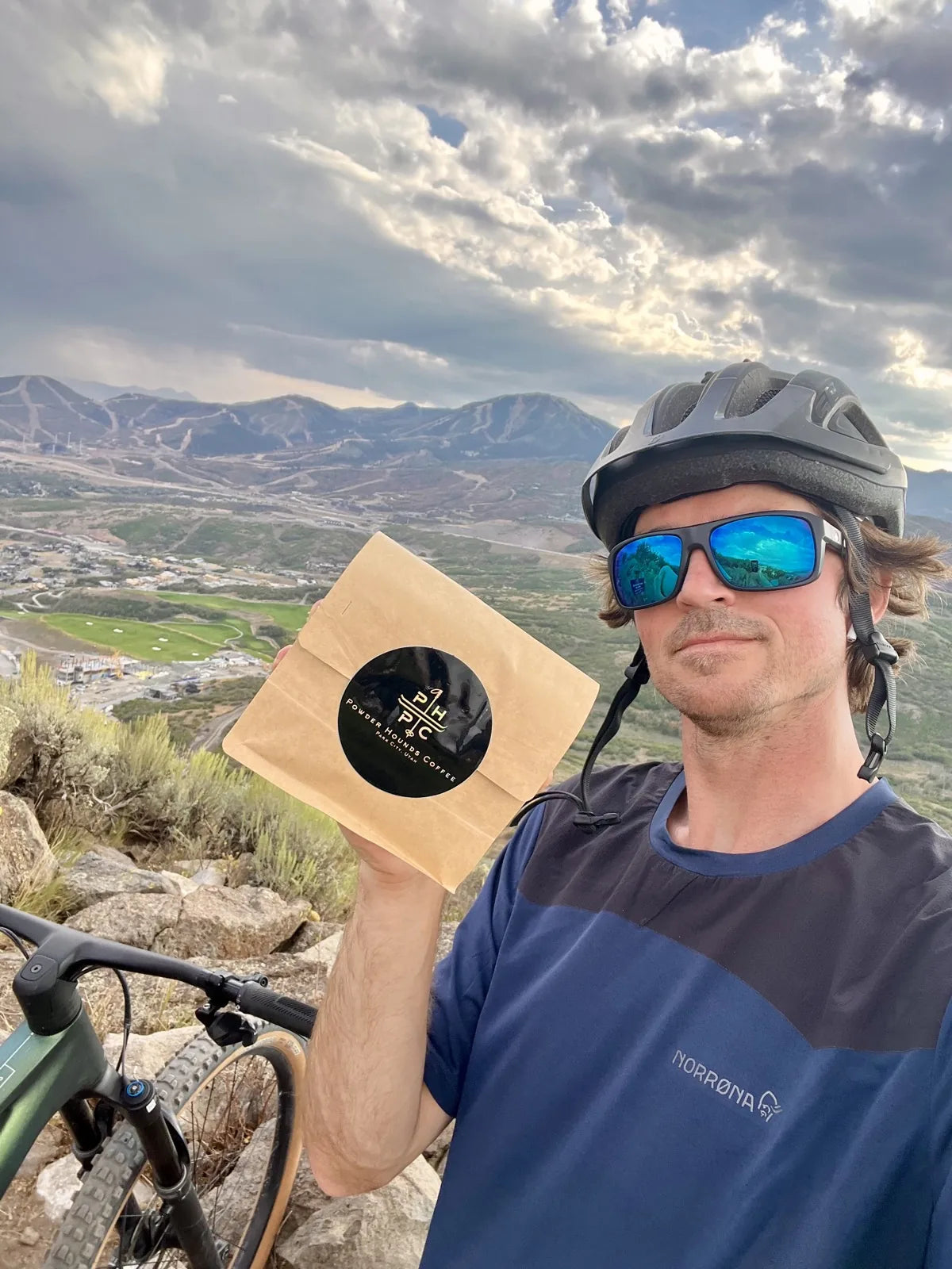 McRae Williams holding a bag of Powder Hounds coffee on a ridge above Park City