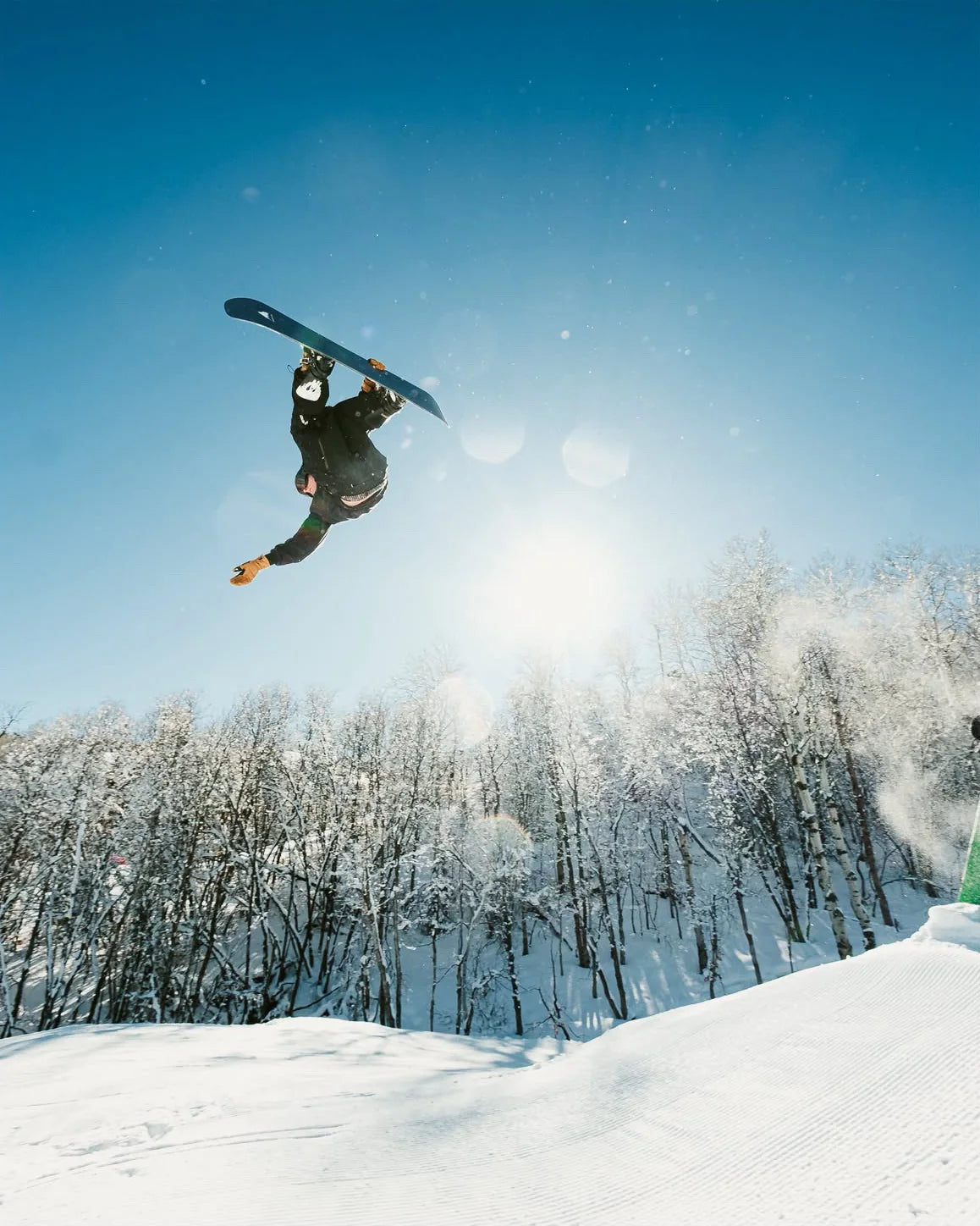 Nate Barber upside down mid-flip on his snowboard above snowy aspens
